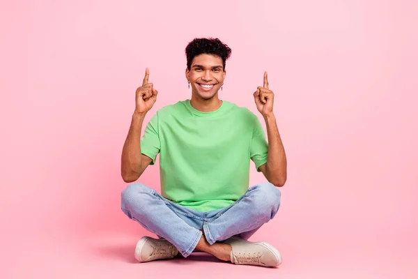 ポジティブな男のフルサイズの写真 緑のTシャツを着て床に座って ピンク色の背景に隔離された空のスペースの提案を示しています — ストック写真