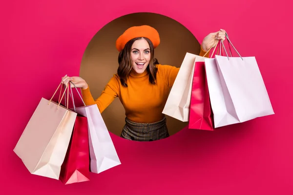 照片上喜形于色的女士从粉红的纸孔里向外张望手拿着一包喜庆买便宜货穿米色背景的衣服 — 图库照片