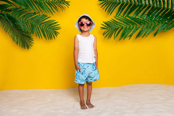 全长照片正面甜小男孩身穿白衬衫深色眼镜享受度假胜地度假孤立的黄色背景 — 图库照片