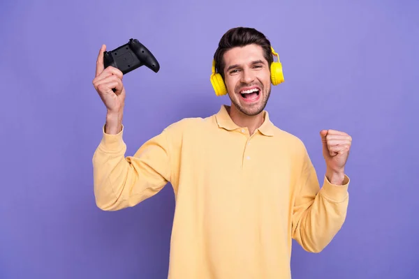 Photo of excited lucky man dressed yellow shirt headphones winning playstation game isolated purple color background.