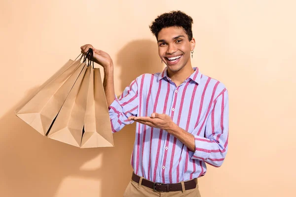 照片上的英俊男子身穿条纹衬衫手掌 头戴非洲裔头发 展示了用米色背景隔离的购物袋 — 图库照片