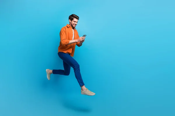 全长照片上精力充沛的有魅力的男人用智能手机跳跑快空出空出的空间广告隔离在蓝色背景下 — 图库照片