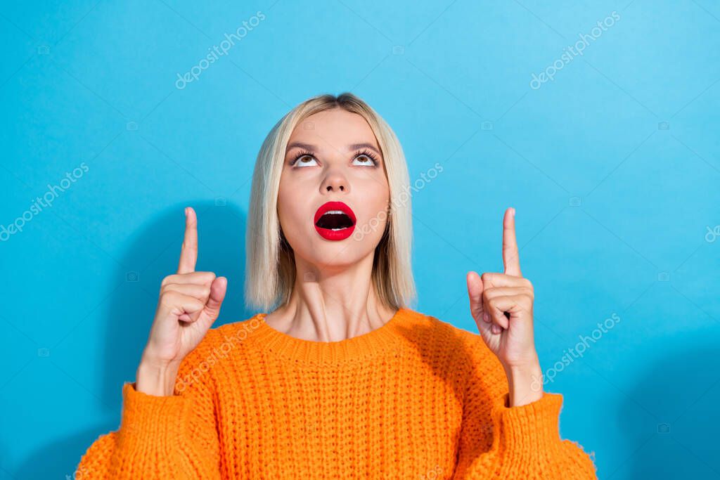 Photo of speechless girl with blond hairdo wear knit orange jumper directing at service empty space isolated on blue color background.