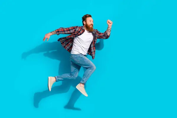 Full body photo of positive man with red beard dressed checkered shirt jeans run shopping in empty space isolated on blue color background.