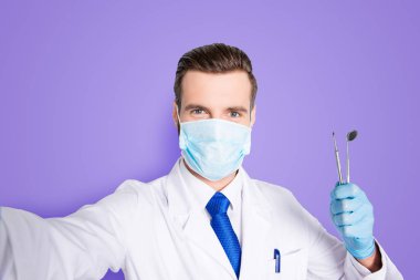 Self portrait of successful cheerful dentist in white lab coat, blue tie, shooting selfie on front camera, holding tools, having leisure, fun, video call, isolated on grey background. clipart