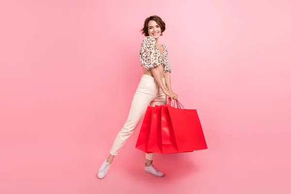 ポジティブなエレガントな女性の完全な長さの写真プリントトップホワイトパンツは ピンク色の背景に隔離されたショッピングバッグに新しい服を保持します — ストック写真