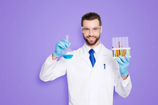 在白色的实验室大衣 戴着带有多色液体的试管和烧瓶的带刚毛的漂亮科学家的肖像 看着在灰色背景下的相机 — 图库照片