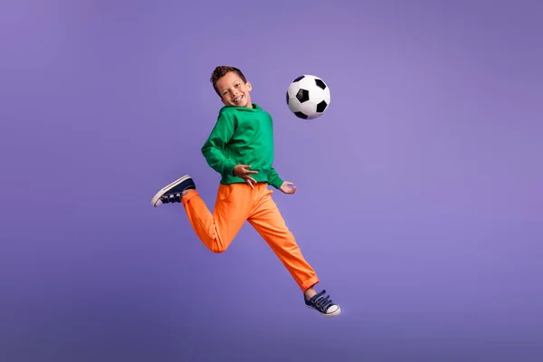 紫色の背景に隔離されたトレーニングフットボールを実行している肯定的な楽観的な少年チームメンバーの写真 — ストック写真