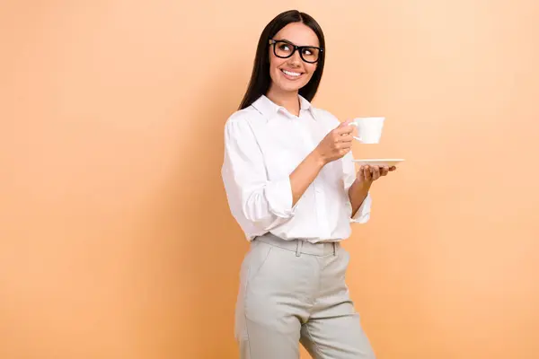 Photo of charming positive minded girl hold espresso coffee cup look empty space ad isolated on beige color background.