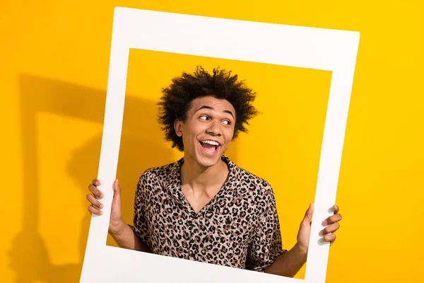 Photo of funky impressed man wear animal print shirt holding paper frame looking empty space isolated yellow color background.