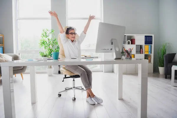 Full length photo of lawyer woman gray hair raised hands up celebrate overjoyed sitting chair work done isolated on home office background.