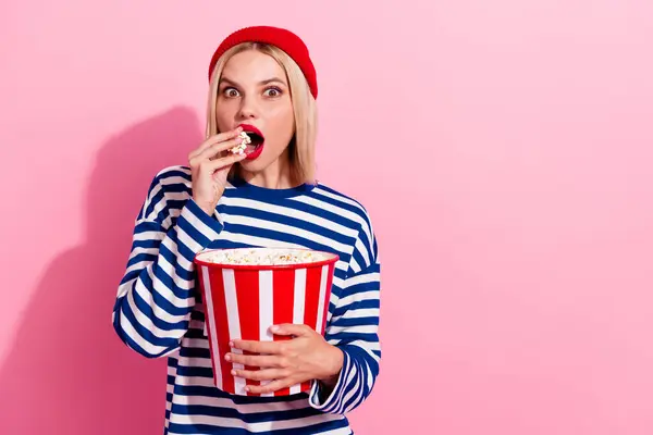 Photo of shocked impressed lady wear striped shirt watching film eating pop corn empty space isolated pink color background.