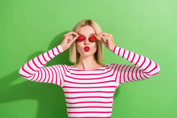 若いポジティブな女性の写真 ブロンドの髪ストライプスタイリッシュなトップキス赤口紅カバー 緑色の背景に隔離されたイチゴ — ストック写真