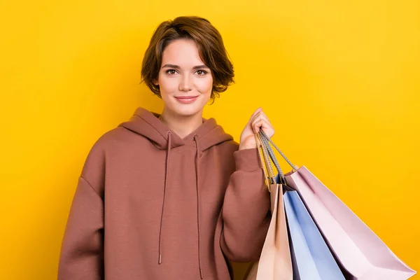 Photo portrait of young charming lady wear brown hoodie hold bargains shopaholic black friday deals isolated on yellow color background.