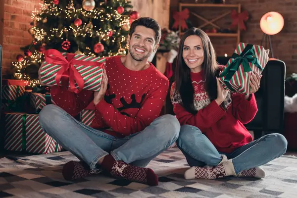 Full body photo of young family dad with mom holding two gifts prepared for their small kids xmas symbol sitting in new year studio.
