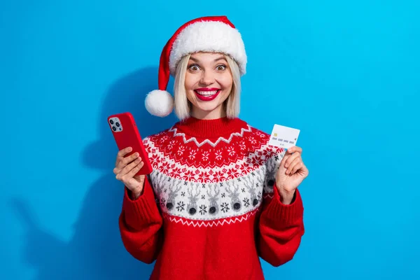 有魅力的人拿着智能手机无线借记卡穿着红色圣诞前夜套头衫 蓝色背景隔离的照片 — 图库照片