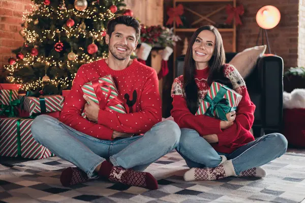 Full body photo of optimistic young family wearing festive red sweaters prepare magic noel holiday night two people indoors sitting carpet.
