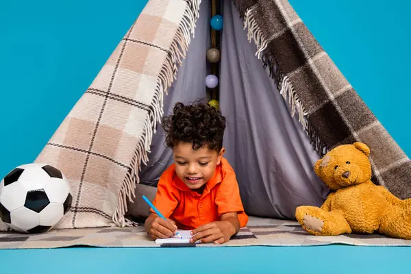 照片上可爱有趣的男孩躺在昏暗的帐篷里 在抄本上写着乳制品 孤立的蓝色背景 — 图库照片