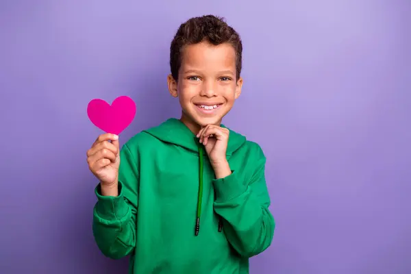 魅力的な思慮深い小さな男の子の写真は 緑のパーカーアーム中国上昇ピンクの紙の心臓を隔離された紫色の背景 — ストック写真
