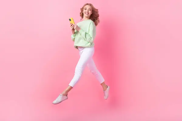 全尺寸肖像兴奋华丽的女孩使用智能电话跳跃跑空空间隔离粉红的背景 — 图库照片