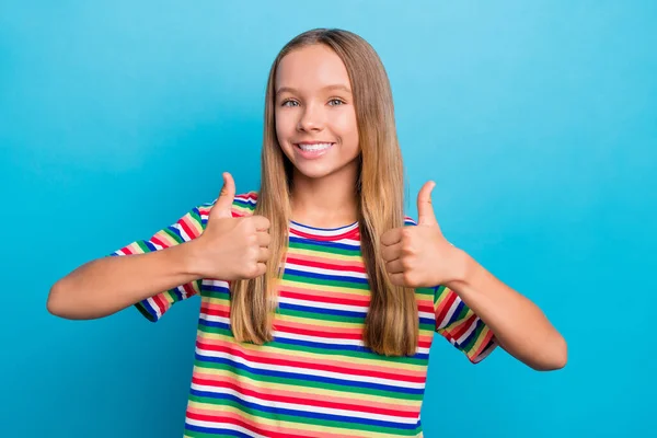 青い色の背景で孤立した親指を示すカラフルなTシャツを着用した満足した10代の少女の肖像画 — ストック写真