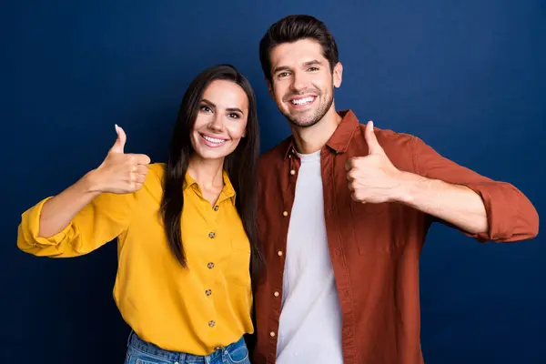 Photo of two cheerful friendly people beaming smile hand finger demonstrate thumb up isolated on blue color background.