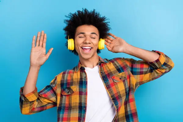 Photo of charming carefree guy dressed checkered shirt dancing closed eyes enjoying music headphones isolated blue color background.