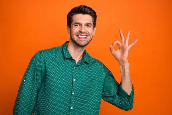 Photo of good mood funky man dressed green shirt showing okey gesture isolated orange color background.