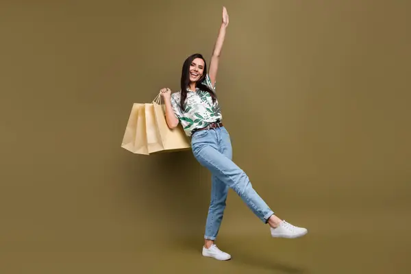 Full size portrait of nice crazy cheerful girl dancing hold mall shop bags isolated on brown color background.