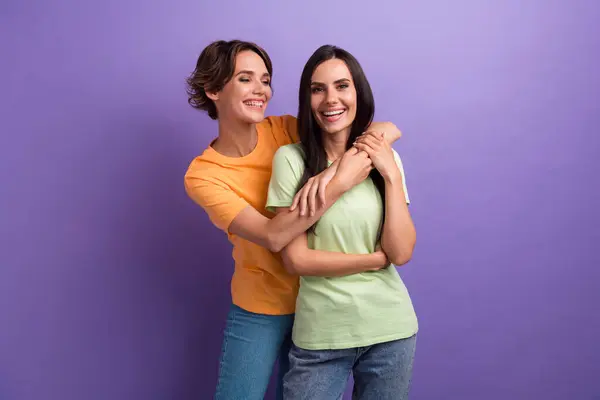 Photo of pretty good mood ladies wear t-shirts smiling cuddling isolated violet color background.