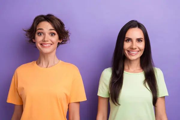 Photo of excited funky ladies wear t-shirts smiling showing white teeth isolated violet color background.