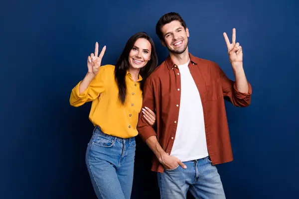 Portrait of two cheerful nice people hold arm fingers demonstrate hello greetings v-sign isolated on blue color background.