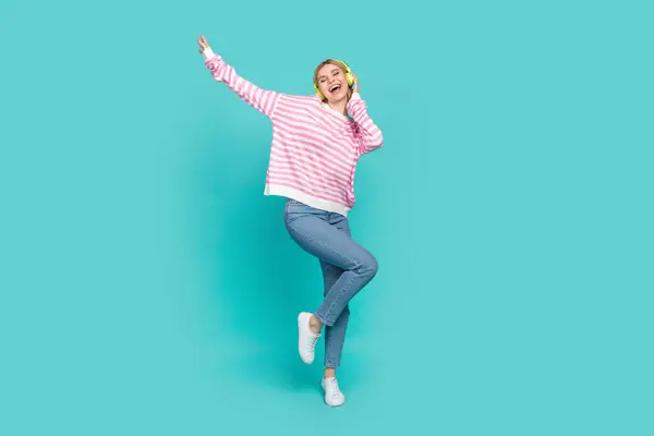 Full body photo of youth dancing woman listen dj music striped pink shirt denim jeans having fun model isolated on cyan color background.