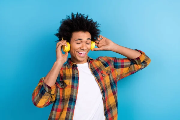 Photo of carefree cheerful guy dressed checkered shirt dancing closed eyes enjoying music headphones isolated blue color background.