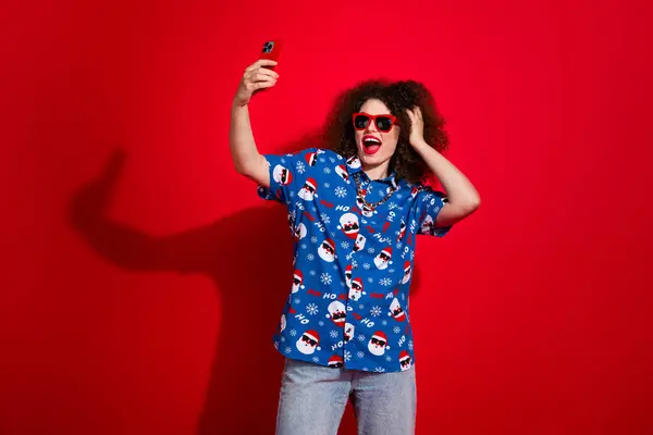 Photo of sweet cool woman wear ugly santa claus print x-mas shirt recording video vlog gadget isolated red color background.