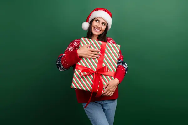 Photo of cute thoughtful woman santa elf wear ornament x-mas pullover hugging gift box empty space isolated green color background.