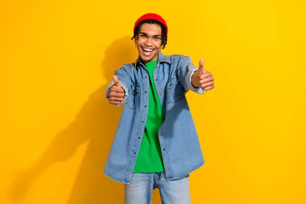 时尚自信的男人身穿牛仔裤衬衫 戴着红色帽子 两个大拇指伸出孤立的黄色背景的照片 — 图库照片