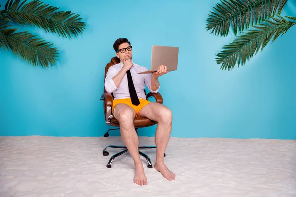 心事重重的商人坐在椅子上用上网本搜索来决定避暑胜地孤立的蓝色海岸背景 — 图库照片