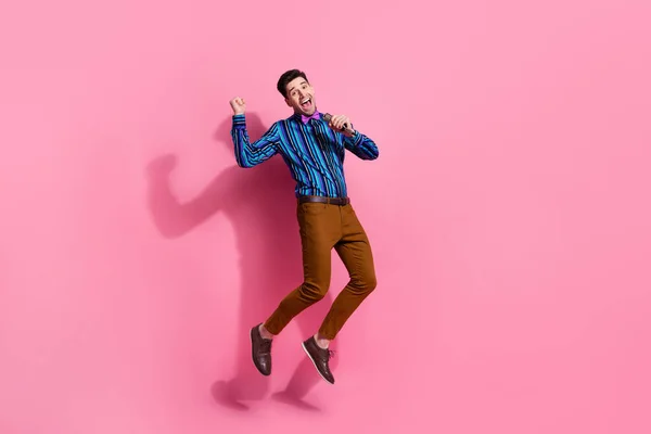 ピンク色の背景に隔離されたガールフレンドのための彼のお気に入りの歌を歌って高いホールディングマイクをジャンプファンキーな男のフルサイズの写真 — ストック写真
