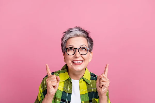 穿着格子衬衫的退休妇女的照片 指向用粉色背景隔开的空空间广告 — 图库照片