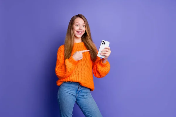 十代の少女の写真はオレンジ色のジャンパーを着用し 指を指す新しいスマートフォンを提供しています 秋の黒の金曜日の販売 バイオレット色の背景で隔離 — ストック写真