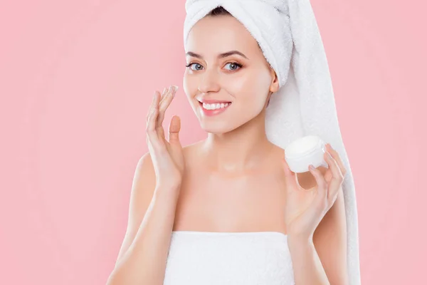 Portrait of charming woman in towel and turban on head, applying face cream for problem combined skin holding bank with balm isolated on white background. Wellness wellbeing concept.