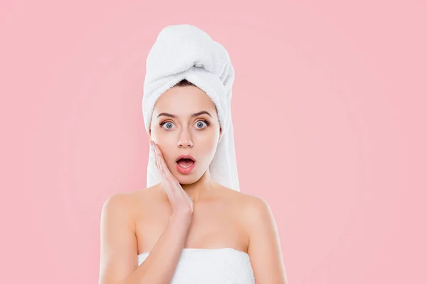 Portrait of frustrated worry woman after shower with towel on head holding hand palm on cheek with wide open mouth and eyes isolated on white background.