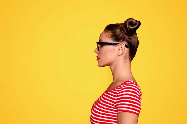 Half-faced side profile view portrait of serious and confident young woman in striped shirt and spectacles isolated on red vivid background with copy space.