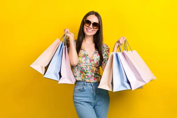 stock image Photo of gorgeous positive cute girl dressed flower print blouse in sunglass holding shopping bags isolated on yellow color background.