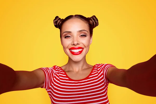 Video call of pretty, charming and smiling young girl with modern hairdo. Model shooting selfie on front camera with two arms isolated on red background.