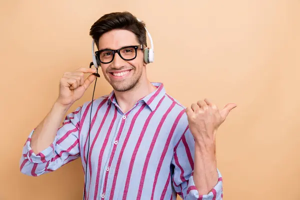 Photo of young sales manager contact with clients using headset touching mic and direct finger mockup isolated on beige color background.