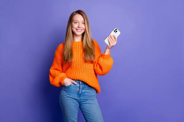 紫色の背景に隔離されたハロウィーンパーティー前に彼女のスマートフォンウェアオレンジジャンパーを使用して陽気な若い十代の少女の写真 — ストック写真