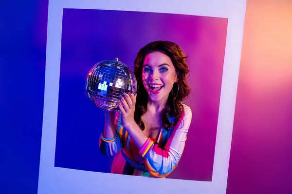 Photo of funky excited lady hands hold glowing disco ball paper album card isolated on pink blue neon background.