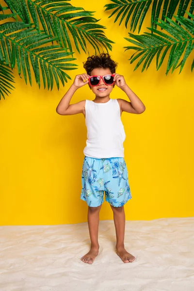 ファンキーなクールな小さな男の子の完全な長さの垂直写真は 休暇を楽しみながら白いシャツのダークアイウェアを着て 隔離された黄色の背景 — ストック写真